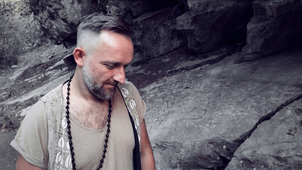 Xaguar in a rocky forest wearing a wooden bead necklace